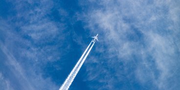 Am Himmel ist ein ganz klein ein Flugzeug zu sehen. Im Vordergrund steht jedoch die Flugspur.