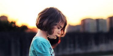 Corona: Kinder leiden unter den Bestimmungen Ein kleines Mädchen mit braunen kurzen Haaren blickt betrübt nach unten.